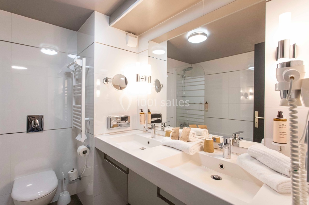 Salle de bain moderne avec double vasque, miroir éclairé, douche vitrée et accessoires de toilette.