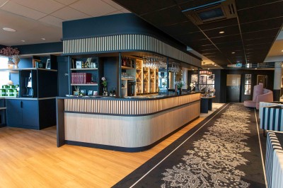 Bureau en bois clair avec une chaise, une machine à café, des tasses et une lampe murale allumée dans une chambre.