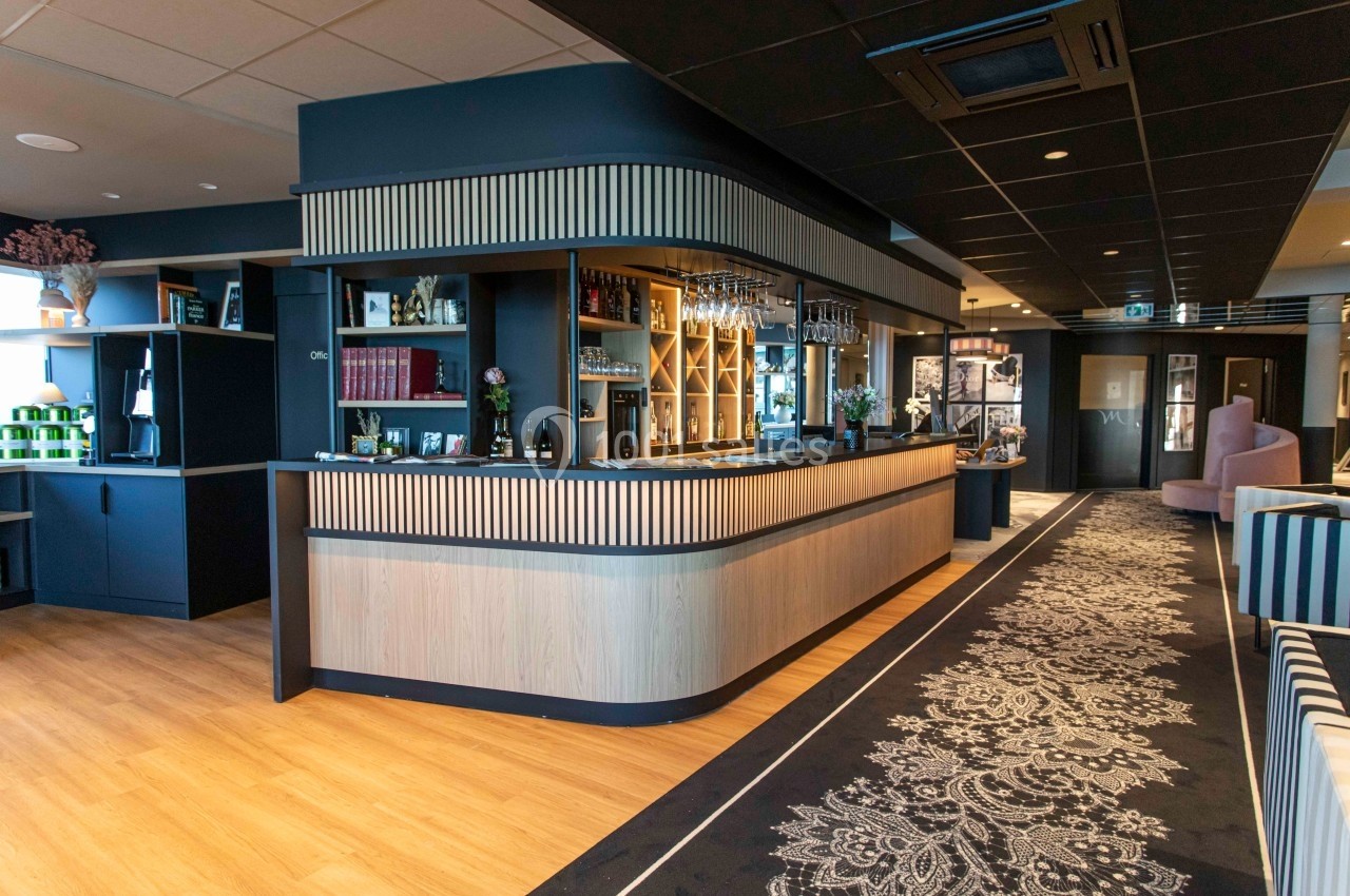 Comptoir de bar moderne en bois clair avec étagères décoratives, dans un espace intérieur élégant et bien éclairé.