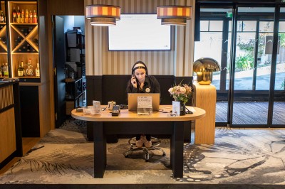 Bureau en bois clair avec une chaise, une machine à café, des tasses et une lampe murale allumée dans une chambre.