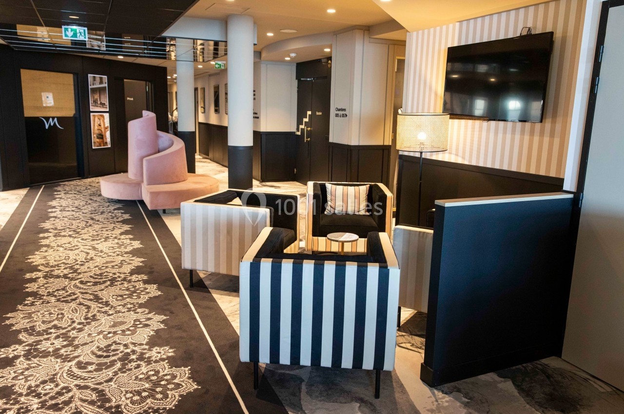 Espace salon avec fauteuils rayés, table basse, lampadaire et télévision, dans un couloir au décor moderne et élégant.