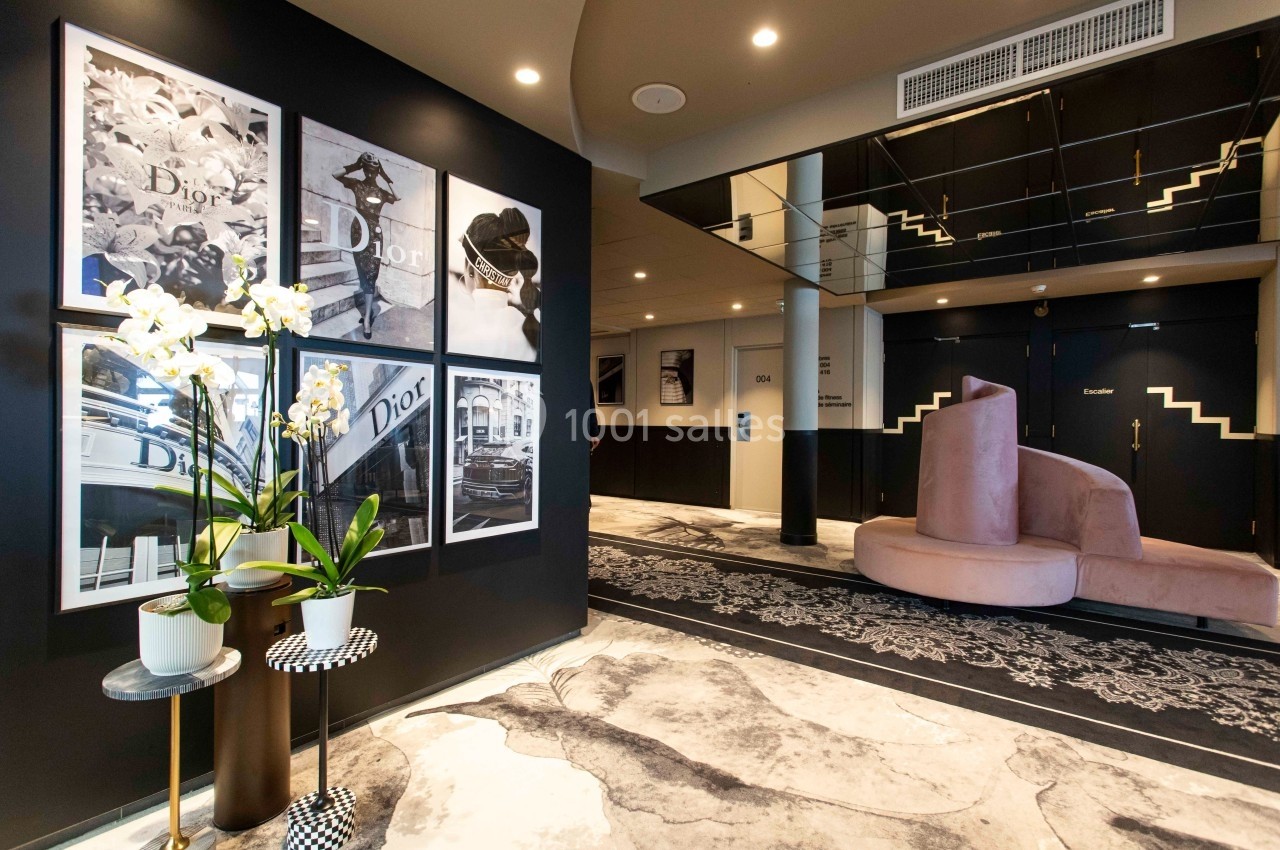 Intérieur d'un espace moderne avec des affiches murales, des orchidées en pot et des sièges rose pâle sur un sol décoratif.