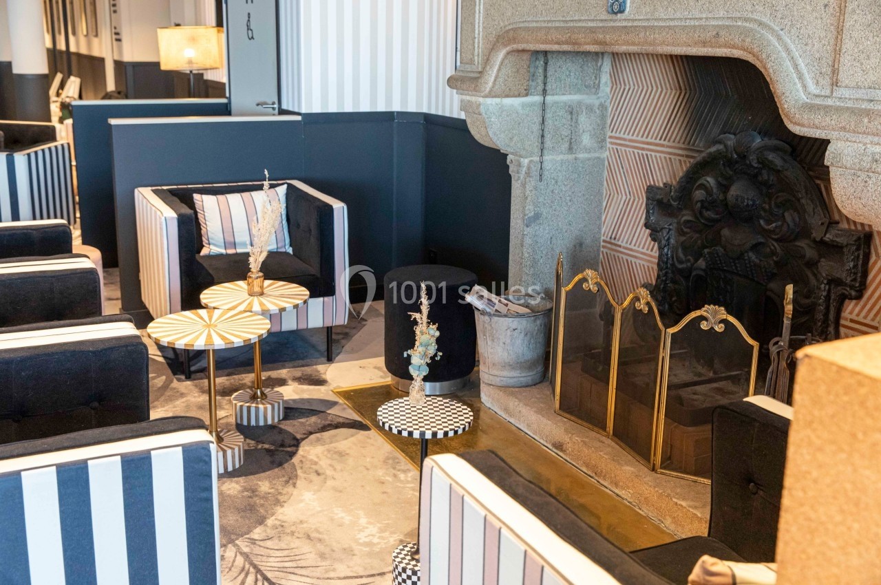 Salon élégant avec fauteuils rayés, tables basses décoratives et cheminée en pierre ornée d'un pare-feu doré.