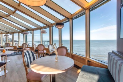 Bureau en bois clair avec une chaise, une machine à café, des tasses et une lampe murale allumée dans une chambre.