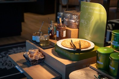Bureau en bois clair avec une chaise, une machine à café, des tasses et une lampe murale allumée dans une chambre.