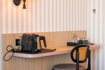 Bureau en bois clair avec une chaise, une machine à café, des tasses et une lampe murale allumée dans une chambre.