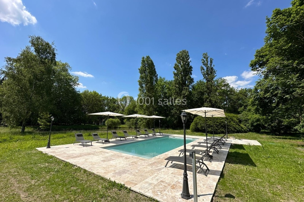 Piscine extérieure entourée de chaises longues et parasols, située dans un jardin verdoyant par temps ensoleillé.