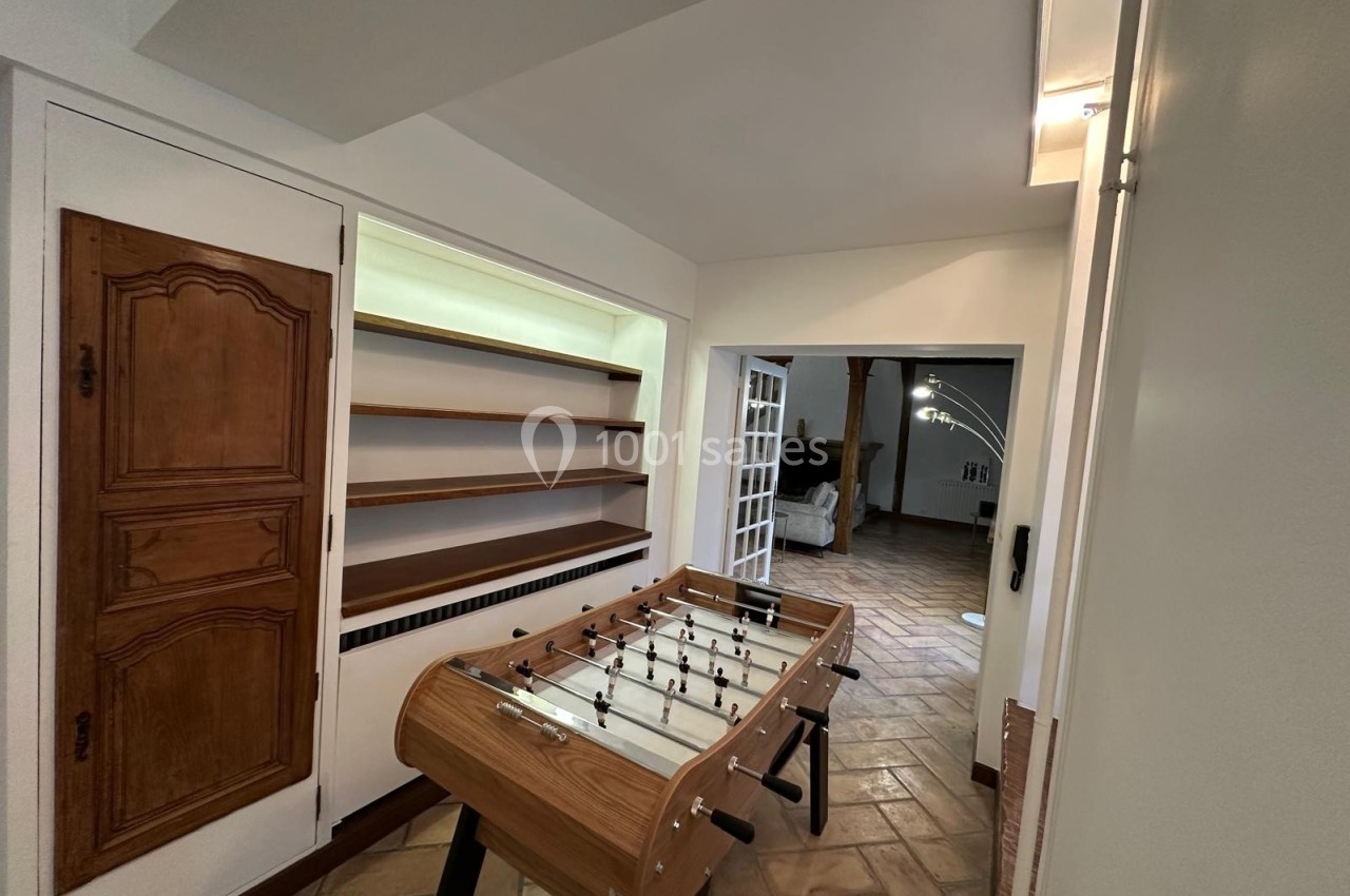 Table de baby-foot en bois placée dans une pièce avec sol en carrelage et étagères murales.