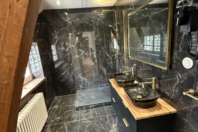 Escalier en bois avec rambarde, dans un intérieur aux murs blancs texturés et sol en carrelage.