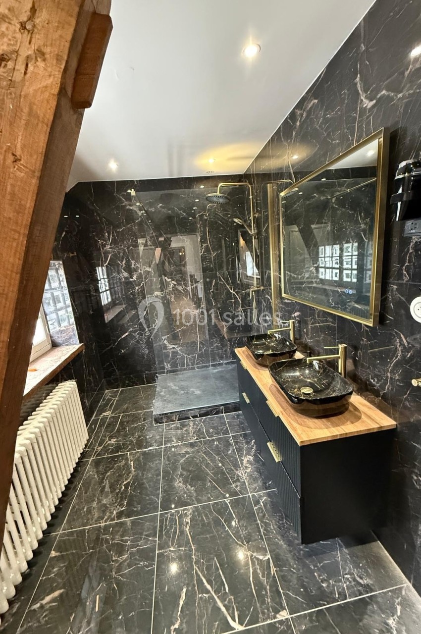 Salle de bain moderne avec murs et sol en marbre noir, double vasque, miroir doré et douche à l'italienne.