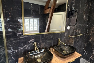 Escalier en bois avec rambarde, dans un intérieur aux murs blancs texturés et sol en carrelage.