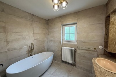 Escalier en bois avec rambarde, dans un intérieur aux murs blancs texturés et sol en carrelage.
