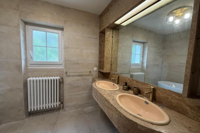 Escalier en bois avec rambarde, dans un intérieur aux murs blancs texturés et sol en carrelage.