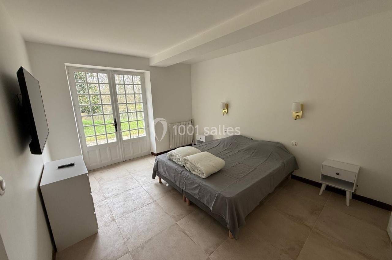 Chambre lumineuse avec un lit double, deux tables de chevet, une télévision murale et une grande porte-fenêtre donnant sur…