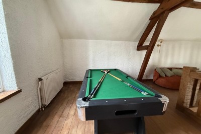 Escalier en bois avec rambarde, dans un intérieur aux murs blancs texturés et sol en carrelage.