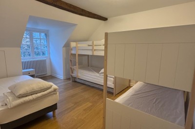 Escalier en bois avec rambarde, dans un intérieur aux murs blancs texturés et sol en carrelage.