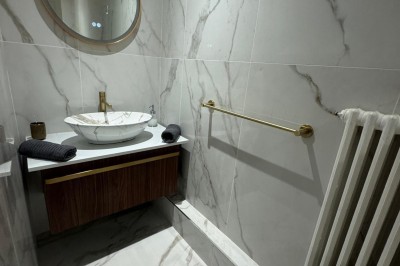 Escalier en bois avec rambarde, dans un intérieur aux murs blancs texturés et sol en carrelage.