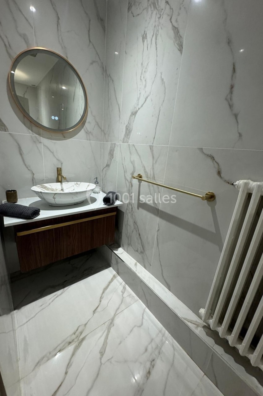 Salle de bain moderne avec lavabo rond, miroir mural, porte-serviettes doré et carrelage effet marbre.