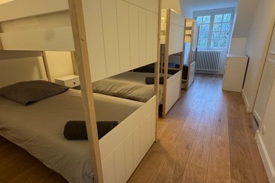 Escalier en bois avec rambarde, dans un intérieur aux murs blancs texturés et sol en carrelage.