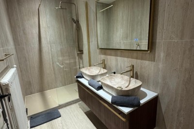 Escalier en bois avec rambarde, dans un intérieur aux murs blancs texturés et sol en carrelage.