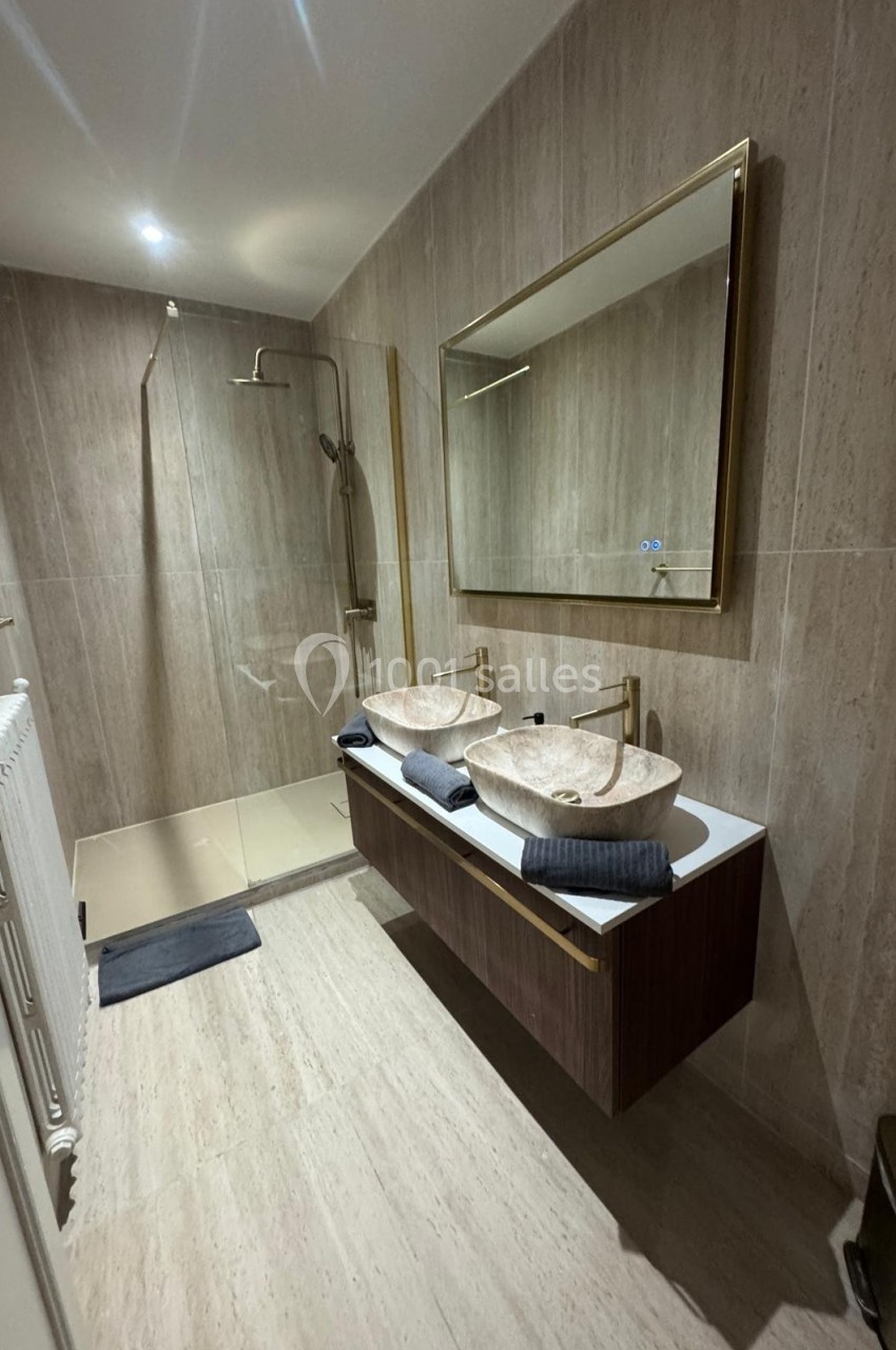 Salle de bain moderne avec douche à l'italienne, double vasque en pierre et miroir encadré doré.