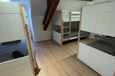 Escalier en bois avec rambarde, dans un intérieur aux murs blancs texturés et sol en carrelage.