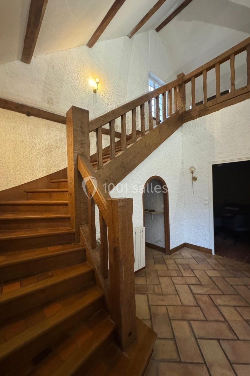 Escalier en bois avec rambarde, dans un intérieur aux murs blancs texturés et sol en carrelage.