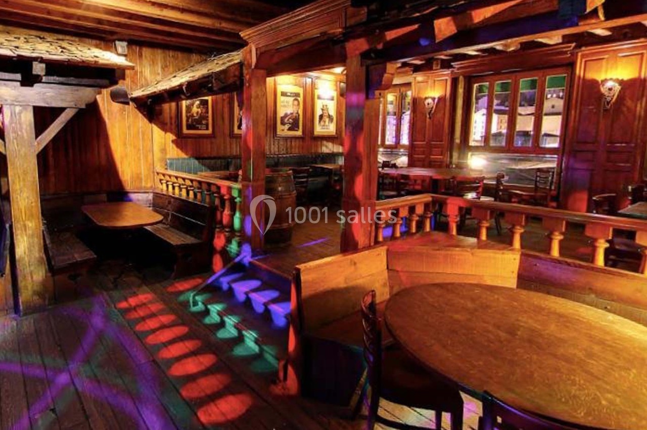 Salle en bois avec tables et chaises, éclairée par des lumières colorées projetant des motifs au sol.