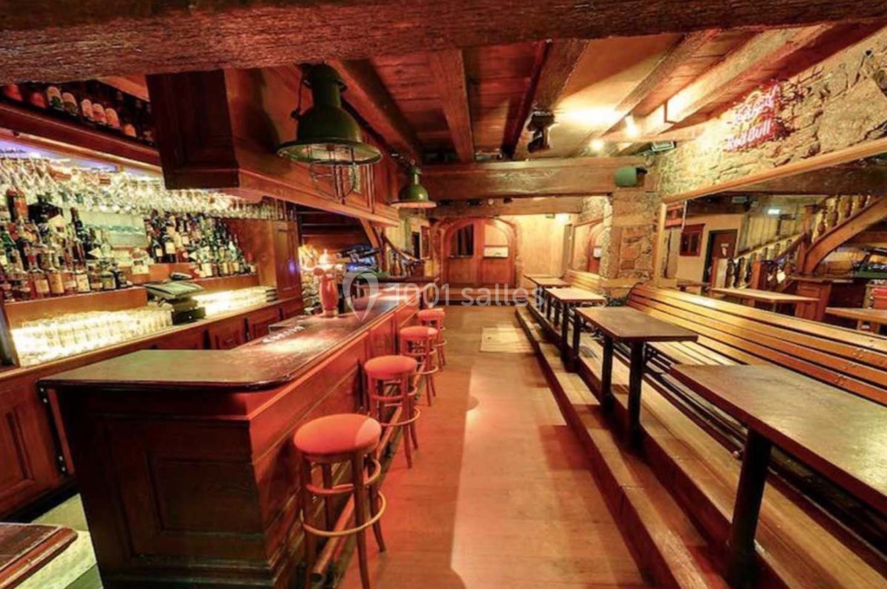 Intérieur d'un bar rustique avec comptoir en bois, tabourets, tables alignées et éclairage chaleureux.