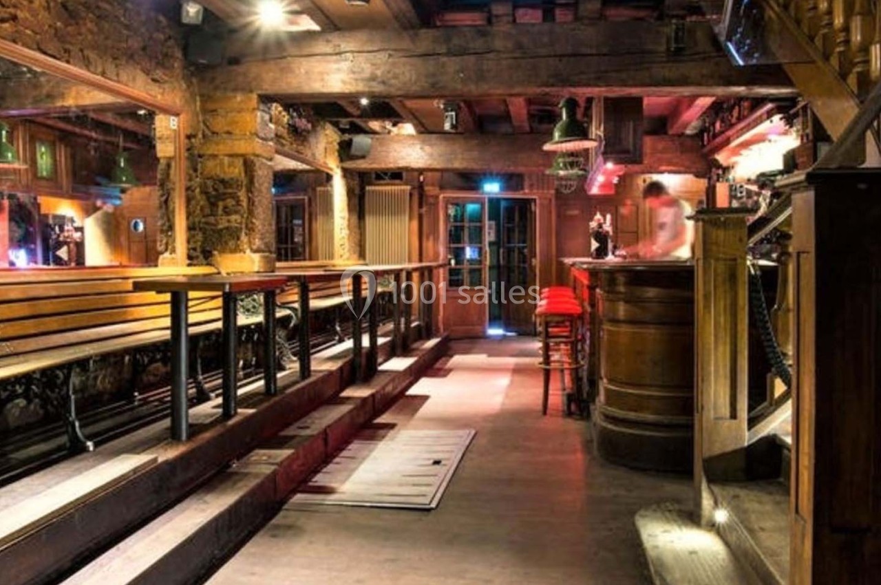 Intérieur d'un bar chaleureux avec des bancs en bois, un comptoir éclairé et une ambiance rustique.