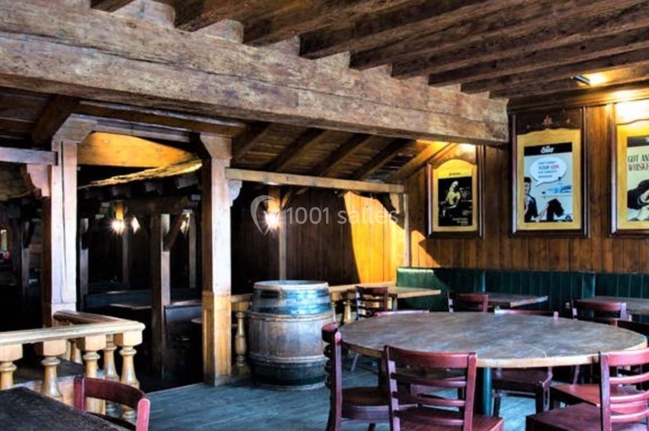 Intérieur d'un pub en bois avec tables, chaises, bar en arrière-plan et affiches encadrées sur les murs.