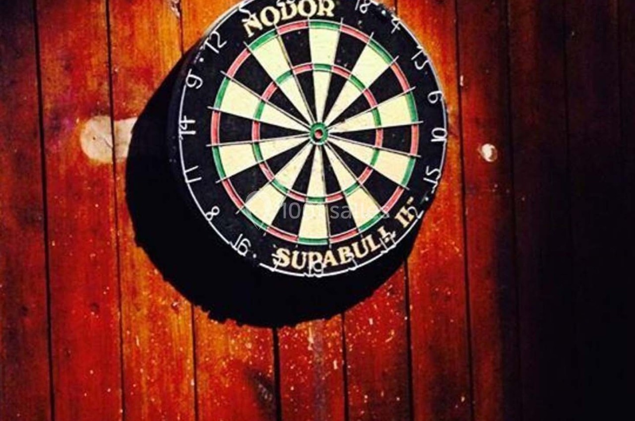 Cible de fléchettes fixée sur un mur en bois, éclairée par une lumière directe.