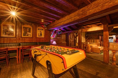 Miniature Salle du Haut Salle en bois chaleureux avec un baby-foot au centre, entourée de tables et chaises, éclairage tamisé.