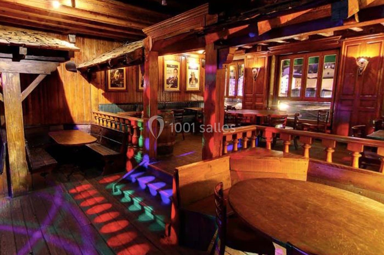 Intérieur d'un bar en bois avec des tables, des bancs et des jeux de lumière colorés sur le sol.