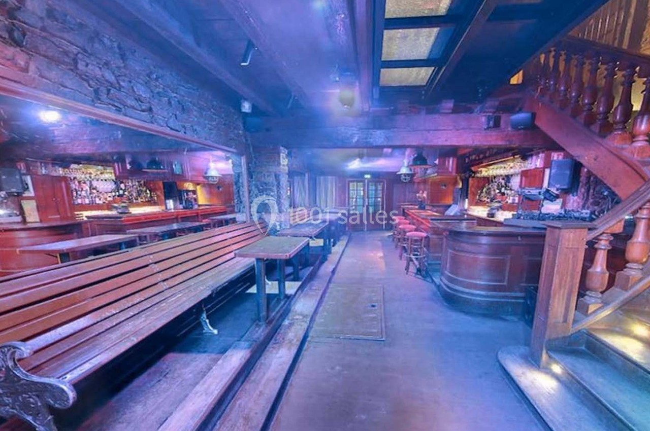 Intérieur d'un pub avec des bancs en bois, un bar en bois sculpté et un éclairage tamisé.
