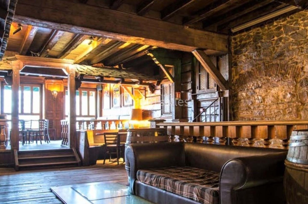 Intérieur d'une pièce rustique avec poutres en bois, murs en pierre, canapé en cuir et lumière naturelle.