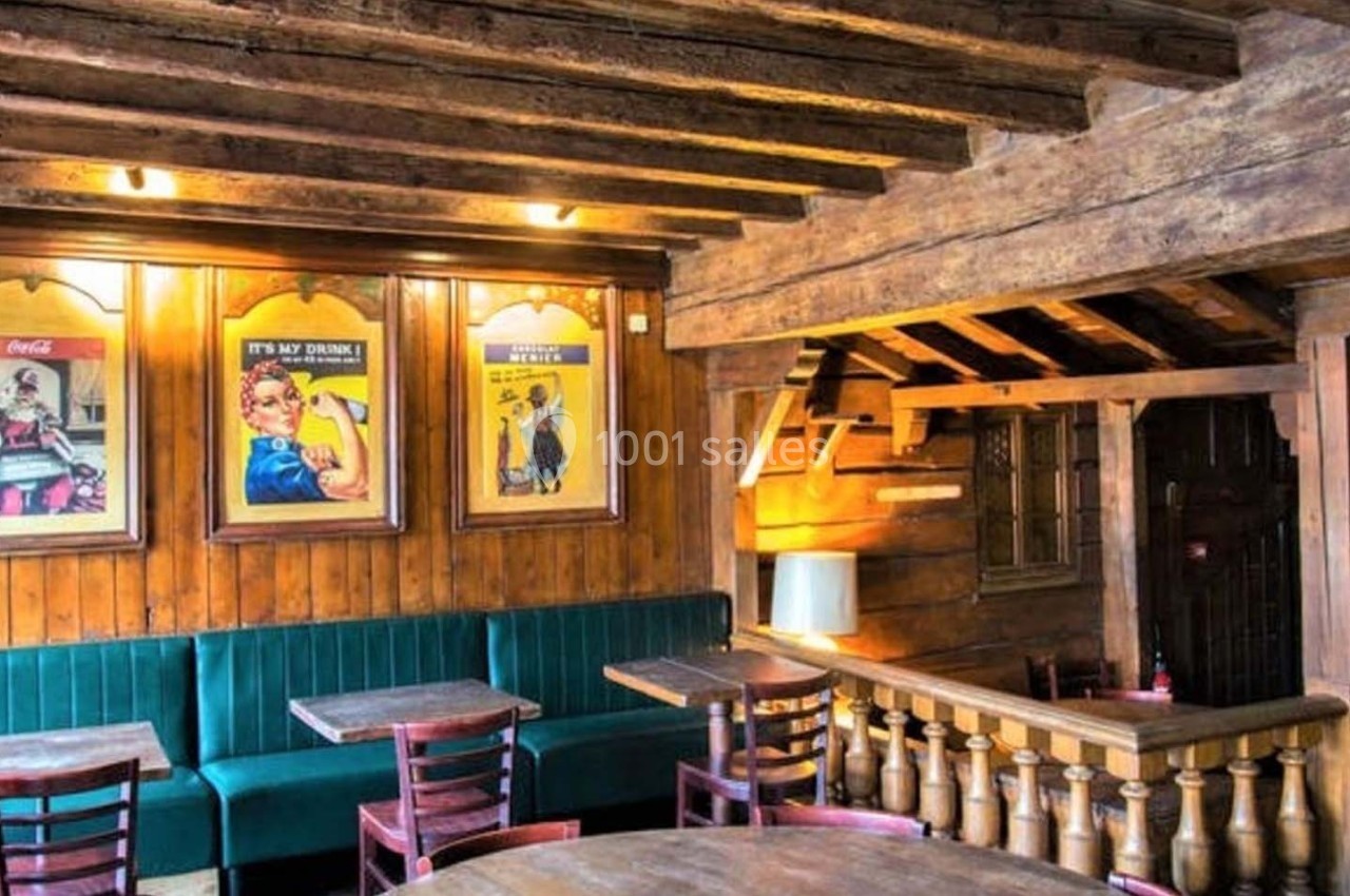 Intérieur d'un café rustique avec poutres en bois, affiches vintage au mur et tables en bois entourées de chaises.