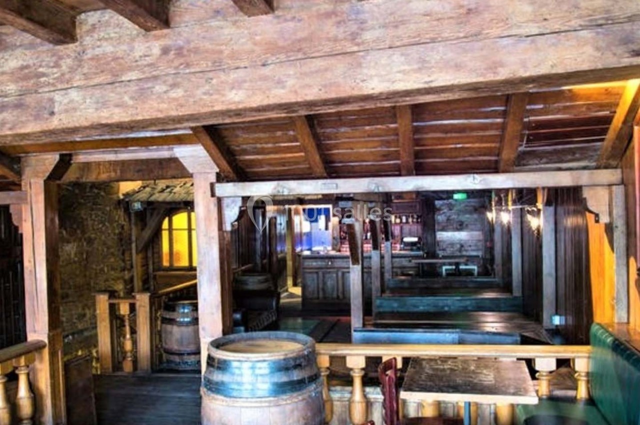 Intérieur d'une taverne en bois avec des tonneaux, des bancs rembourrés et une ambiance rustique chaleureuse.