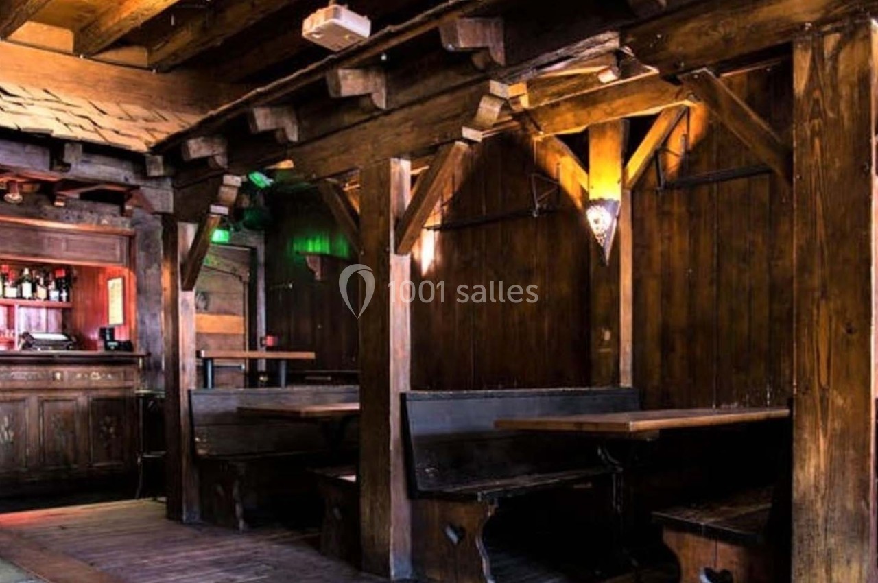 Intérieur d'un bar en bois avec des tables, des bancs et un comptoir éclairé par des lumières tamisées.