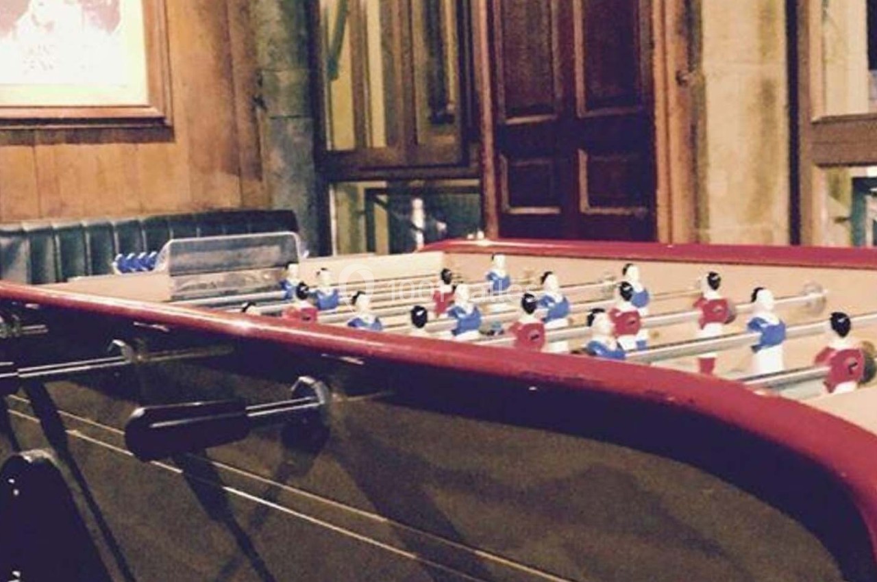 Table de baby-foot dans un intérieur en bois avec banquettes et fenêtres donnant sur l'extérieur.