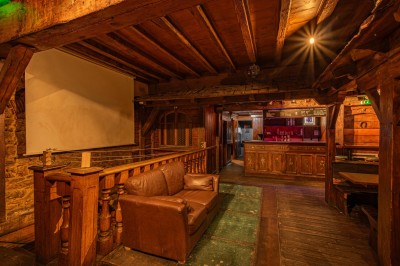 Miniature Salle du Haut Salle en bois chaleureux avec un baby-foot au centre, entourée de tables et chaises, éclairage tamisé.