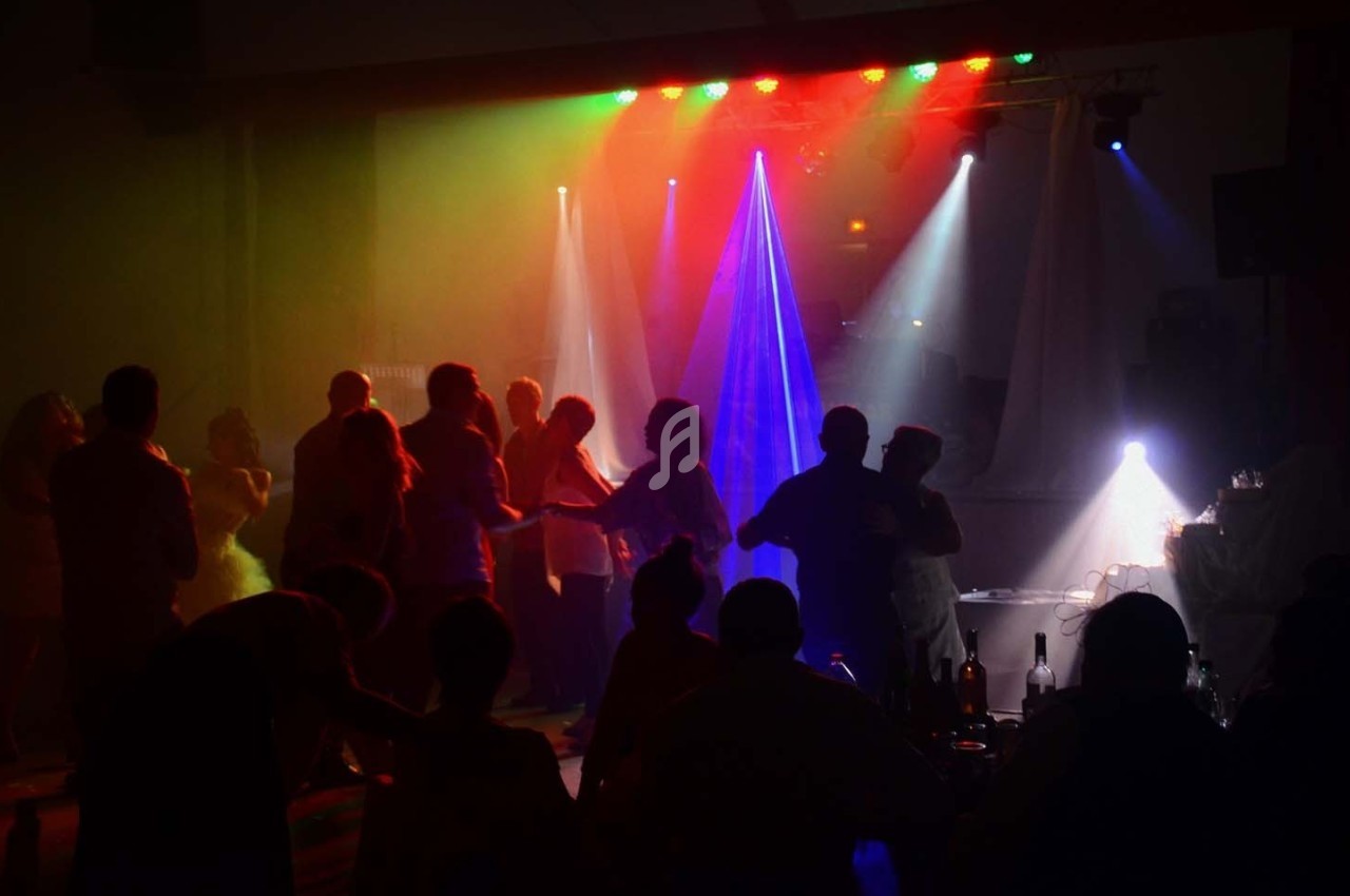 Des silhouettes dansent dans une salle sombre éclairée par des lumières colorées et des projecteurs.
