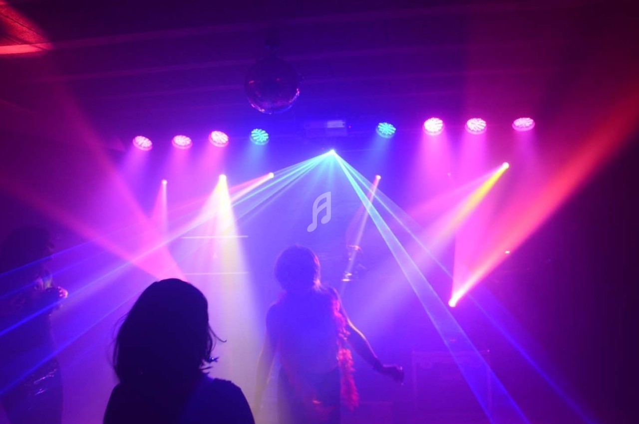Personnes dans une salle sombre éclairée par des faisceaux lumineux colorés et des projecteurs.