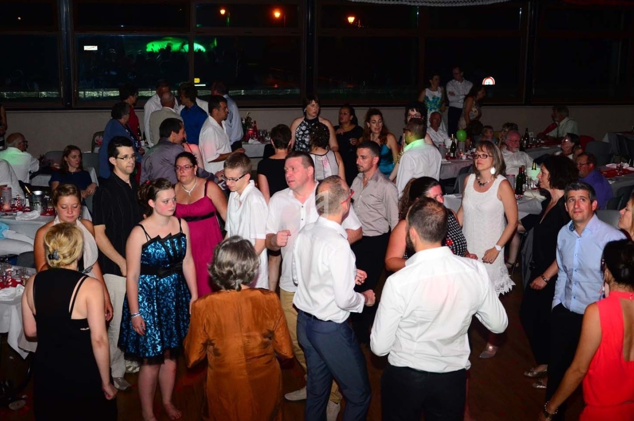 Personnes dansant et discutant dans une salle de réception éclairée, avec des tables dressées en arrière-plan.