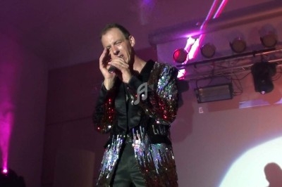 Un homme chante sur scène avec un micro, éclairé par une lumière rouge dans une ambiance sombre.