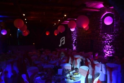 Salle de réception décorée avec des lanternes rouges suspendues, éclairage violet et tables dressées pour un événement.