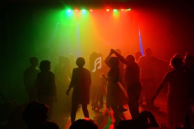 Personnes dansant dans une salle sombre éclairée par des lumières colorées rouge, verte et bleue.