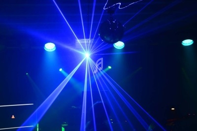 Jeux de lumières bleues et lasers projetés dans une salle sombre avec une boule disco suspendue.