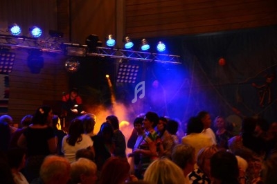 Groupe de personnes dansant sous des lumières colorées lors d'une soirée festive en intérieur.