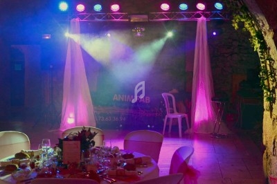 Scène éclairée avec des projecteurs colorés, rideaux blancs et table dressée au premier plan dans une salle de réception.